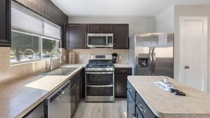 A modern kitchen with dark cabinets, stainless steel appliances, and a window providing a view of parked cars. - Chic Contemporary Home w/ Park + Garage/Pets ok (Conroe)