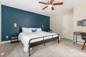 Ein Schlafzimmer mit Bett, Schreibtisch, Deckenventilator und Wand mit geometrischem Muster.