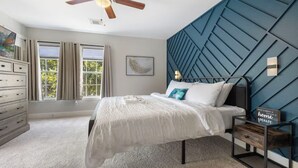 A bedroom with a bed, a nightstand, a ceiling fan, a dresser, and a window with curtains. - Chic Contemporary Home w/ Park + Garage/Pets ok (Conroe)