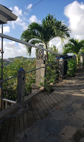 Eine Steintreppe führt zu einer Terrasse mit Blick auf ein Wohngebiet und eine Palme.