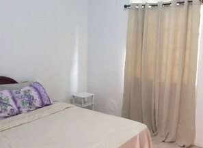 A bedroom with a bed, a nightstand, and a window with beige curtains. - 2-bedroom apartment in Brighton Beach with stunning views & AC for relaxing stay (Brighton)