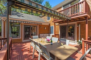 Una terraza de madera con una mesa y sillas, un sofá y una pérgola con toldo a rayas.