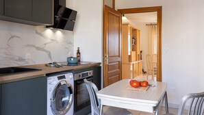 A compact kitchen with a washing machine, a sink, and a table with tomatoes. - Casa Luiggina – Appartement de charme avec vue mer au cœur de L’Île-Rousse (L'Île-Rousse)