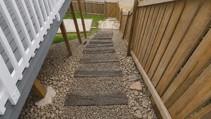 Un pontile in legno con ringhiera bianca, scalini in legno e un vialetto sterrato che porta a un cancello.