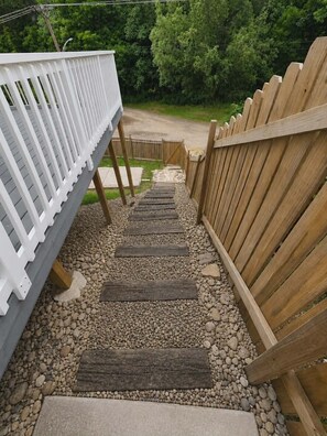Eine Holzterrasse mit weißer Geländer, Holzstufen und einem Kiesweg, der zu einem Tor führt.