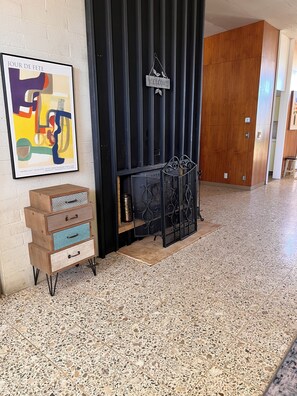 Un pasillo con una reja de metal negro, un letrero de bienvenida, una obra de arte abstracta enmarcada y un mueble de madera con cajones.