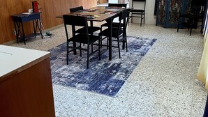 A dining area with a wooden table, black chairs, a blue patterned rug, and a tiled floor.