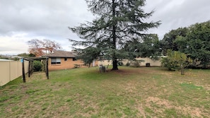 A backyard with a large tree, a patio table, and a house.