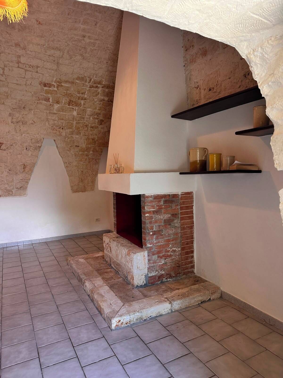 Una cocina con un horno de ladrillo, estantes con utensilios de cocina y piso de baldosas.