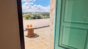 A door leading to a balcony with a view of a rural landscape, a small round table, and potted plants. - Giardino dei Trulli Cummerse (Castellana Grotte)