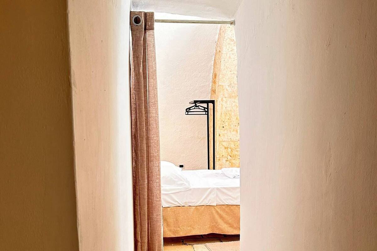 Un pasillo estrecho que conduce a un dormitorio con cama, perchero y suelo de losas de piedra.