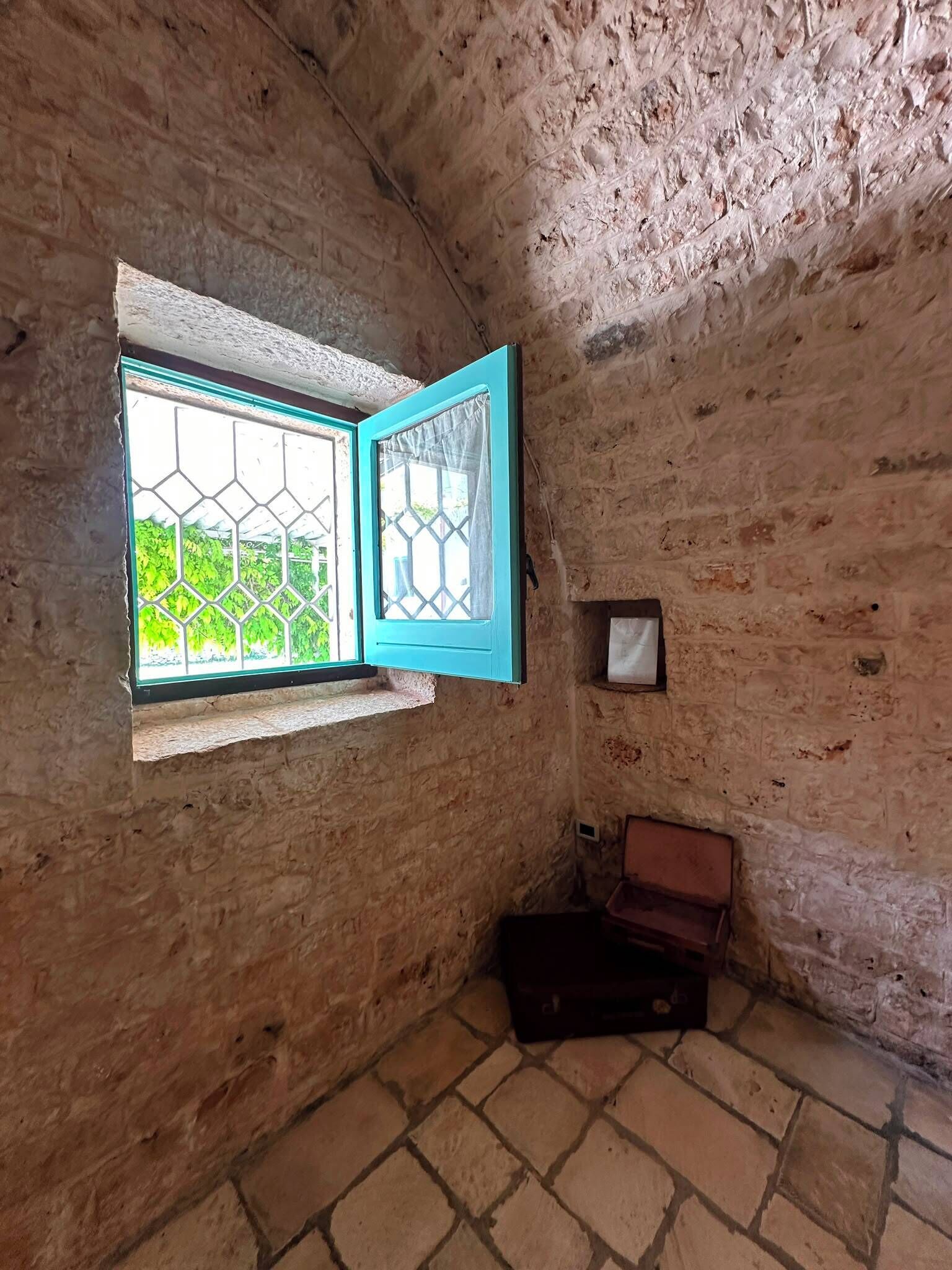 Una habitación con ventana, una pequeña estantería y una maleta.