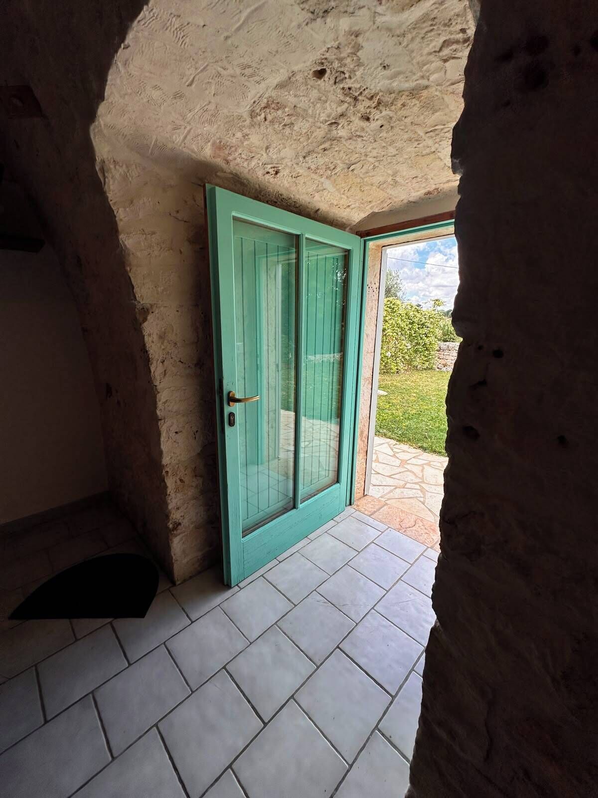 A room with a teal door, stone walls, and a tiled floor.
