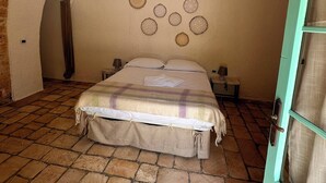 A bedroom with a stone floor, a bed with a plaid blanket, a hanging lamp, and a wall with circular decorations. - Giardino dei Trulli Cummerse (Castellana Grotte)