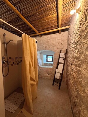 A stone-walled bathroom with a shower, a window, and a wooden ladder. - Giardino dei Trulli Cummerse (Castellana Grotte)