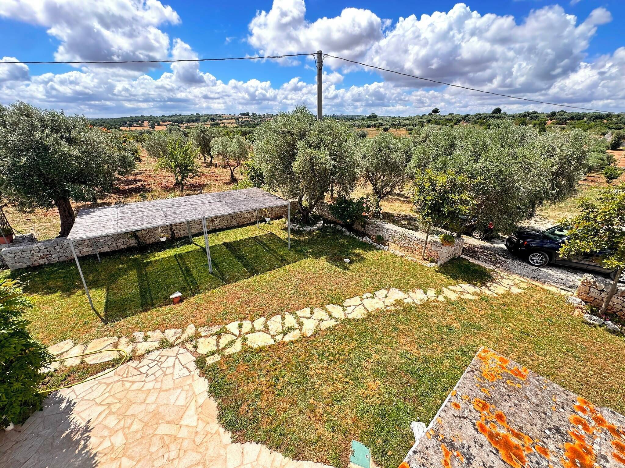 Un jardí amb camins de pedra, una pèrgola i oliveres.