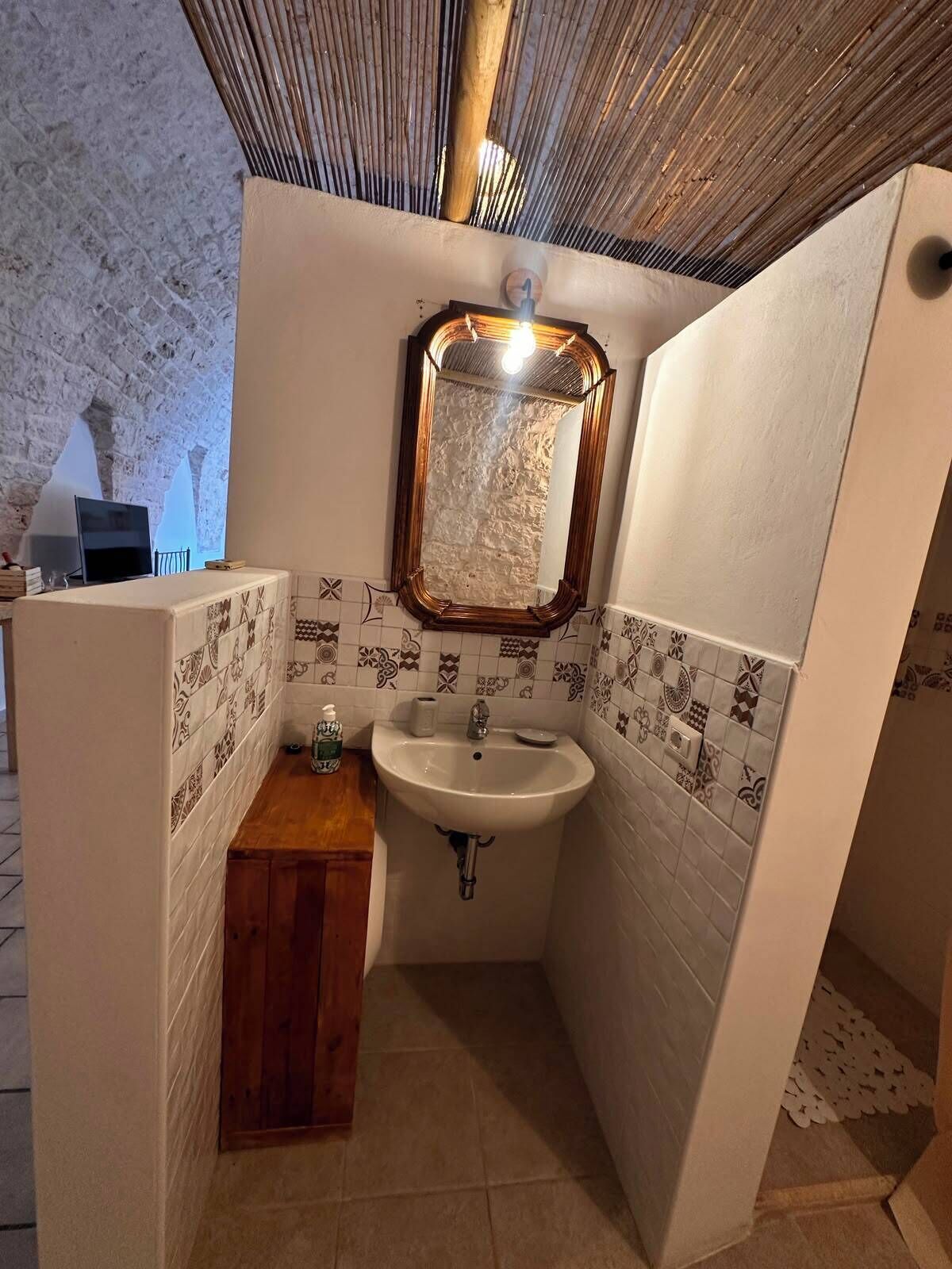 Un baño con un lavabo blanco, un mueble de tocador de madera, un espejo con marco de madera y azulejos estampados en las paredes.