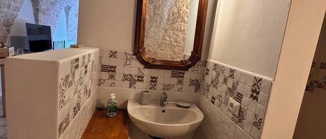 Un baño con un lavabo blanco, un mueble de tocador de madera, un espejo con marco de madera y azulejos estampados en las paredes.