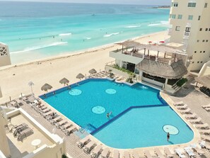 A pool with a view of the beach and ocean, surrounded by lounge chairs and umbrellas. - Ventanas al Paraiso Apartments Cancun (Cancun)