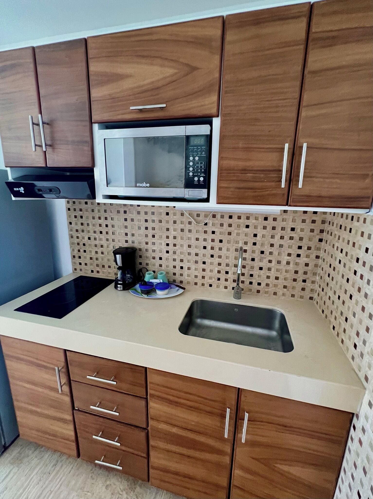 Una cocina con armarios de madera, microondas, fregadero y cafetera.