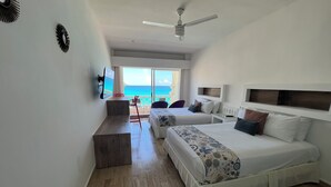 Habitación de hotel con dos camas, un escritorio, una silla, un televisor y un balcón con vistas al océano.