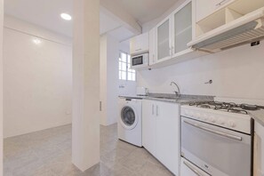 A compact kitchen with a washing machine, microwave, and gas stove. - MOT Rentals + Junin - 2 Bd (Buenos Aires)