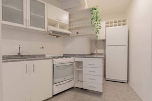 A kitchen with white cabinets, a stove, a refrigerator, and a hanging plant. - MOT Rentals + Junin - 2 Bd (Buenos Aires)