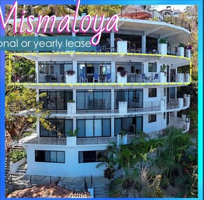 A multi-story building with balconies, large windows, and outdoor plants.