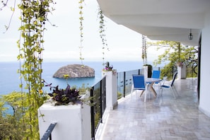 Ein Balkon mit Meerblick, einem Tisch mit Stühlen und einer hängenden Pflanze.