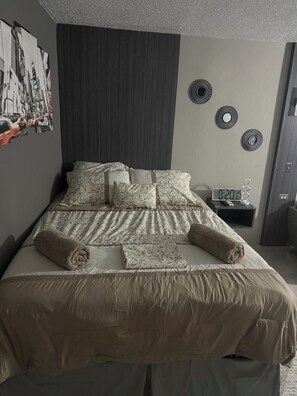 Una cama bien hecha con ropa de cama estampada, un cabecero oscuro y decoración de pared.