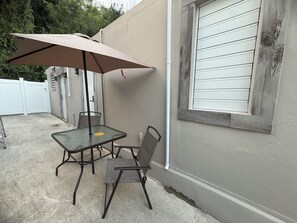 Eine Terrasse im Freien mit Tisch und Stühlen, einem Sonnenschirm und einem weißen Zaun im Hintergrund.