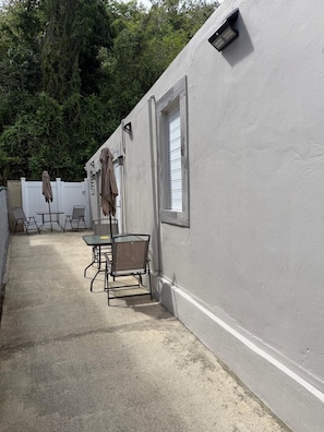 Un patio con mesa y sillas, una ventana y una pared blanca.