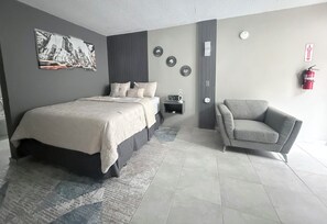A modern bedroom with a bed, a gray armchair, a nightstand, a wall clock, and a fire extinguisher. - GOLDEN SECRETS 3 (YOUR MODERN CORNER) (San Antonio)