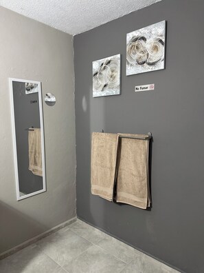 Un baño con espejo, dos toallas y tres obras de arte colgadas en la pared.