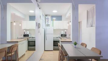 Una cocina compacta con gabinetes blancos, un refrigerador, una estufa y un microondas. Hay una mesa de comedor con sillas y una pequeña planta en maceta.