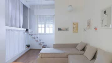 A modern living room with a sofa, a staircase, and artwork on the walls.