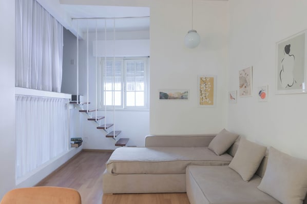 Una sala de estar moderna con un sofá, una escalera y obras de arte en las paredes.
