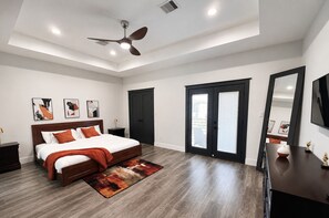 A bedroom with a bed, a ceiling fan, a nightstand, a dresser, a mirror, and a door with a glass panel. - FIFA 2026 •  Luxury 3BR with King Suite • balcony (Houston)