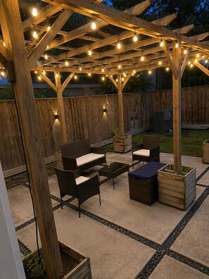 Ein überdachter Patio-Bereich mit Holzmöbeln, Lichterketten und Pflanzgefäßen.