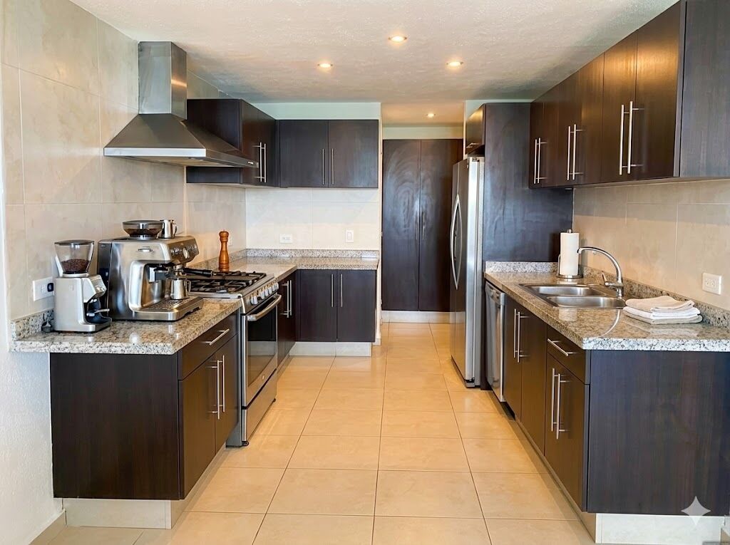 A modern kitchen with dark cabinetry, stainless steel appliances, and a granite countertop.