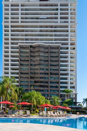 A high-rise hotel with multiple balconies, a swimming pool, and red umbrellas. - Gran Venetian Resort Stay Oceanfront by Monyxbnb (Puerto Vallarta)