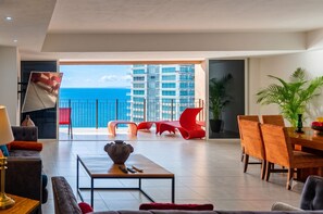 En moderne stue med balkon, røde stole, et spisebord og havudsigt.