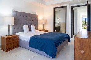 Moderni hotellihuone, jossa on suuri sänky, kaksi yöpöytää, vaatekaappi ja kylpyhuone, joka näkyy avoimesta ovesta.