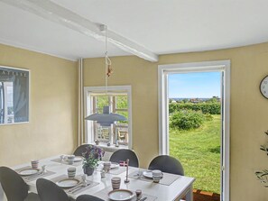 Ein Essbereich mit einem Tisch für vier Personen, einer Hängeleuchte, einem Fenster mit Blick auf Grünflächen und einer Wanduhr.