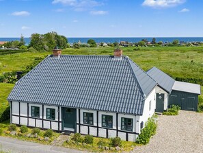 Ein traditionelles Fachwerkhäuschen mit grau schiefergedecktem Dach, einem kleinen angebauten Schuppen und Blick auf das Meer.