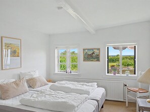 Ein Schlafzimmer mit zwei Betten, einem Heizkörper, einem Sessel und Blick auf Grün durch die Fenster.