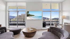 Ein modernes Wohnzimmer mit großen Fenstern, einem Flachbildfernseher, grauen Sofas und einem Couchtisch aus Holz.