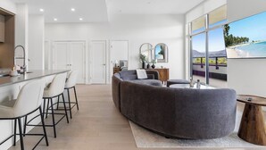 Ein modernes Interieur mit einer Küche, Essbereich und Sitzgelegenheiten, wobei ein großes Fenster den Blick ins Freie bietet.