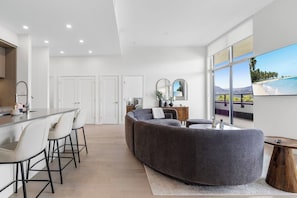 A modern interior with a kitchen, dining area, and seating with a large window offering a view.