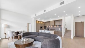 Ein modernes Wohnzimmer mit einer gebogenen grauen Couch, einem Holztisch und einem Essbereich mit Stühlen und einer Lampe.